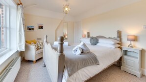 A bedroom with a bed, bedside tables, a window with curtains, a radiator, a mirror, and a chandelier. - 2 Bed in Walberswick (oc-grs) (Walberswick)