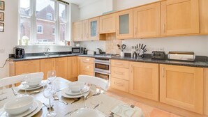 A modern kitchen with wooden cabinets, a dining table set for four, and a large window providing natural light. - 2 Bed in Southwold (oc-sl135) (Southwold)