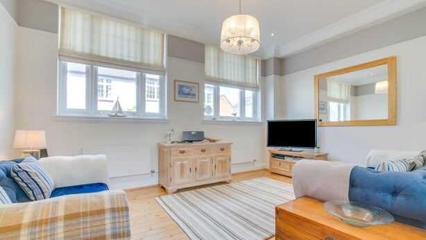 A living room with a sofa, a television, a wooden cabinet, and a large mirror. - 2 Bed in Southwold (oc-sl135) (Southwold)