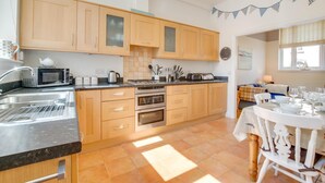 A modern kitchen with wooden cabinets, a built-in oven, a microwave, and a dining area with a table set for four. - 2 Bed in Southwold (oc-sl135) (Southwold)