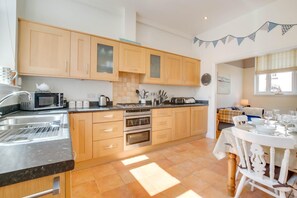 A modern kitchen with wooden cabinets, a built-in oven, a microwave, and a dining area with a table set for four. - 2 Bed in Southwold (oc-sl135) (Southwold)