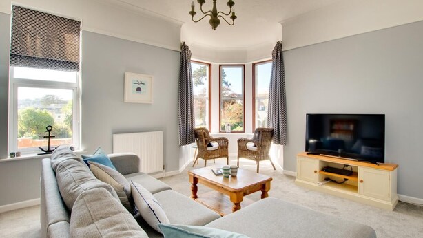 A living room with a sofa, two armchairs, a coffee table, a TV, and a bay window with curtains.
