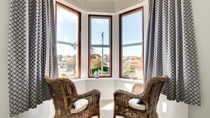 A corner room with two wicker chairs, a bay window, and patterned curtains.