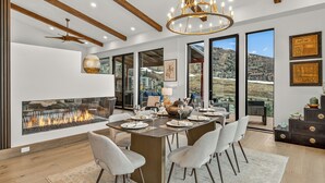 A modern dining room with a fireplace, large windows, and a chandelier. - Bold Views, Bright Spaces | Nocturne View (Steamboat Springs)