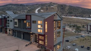 A modern multi-story building with a mix of architectural styles, including a prominent red and grey facade, large windows, and a sloped roof. - Bold Views, Bright Spaces | Nocturne View (Steamboat Springs)