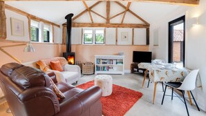 A cozy living room with a fireplace, leather sofa, white armchair, and a dining area with a table and chairs.