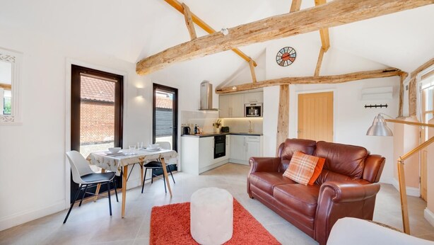 A spacious living area with a dining table, leather sofa, and a kitchen in the background.