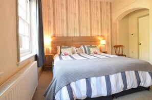 A bedroom with a large bed, wooden headboard, two bedside lamps, a chair, and a radiator. - 5 Bed in Studland (oc-wy365) (Studland)