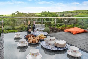 A table set for a meal with plates, glasses, and a bottle of wine on a balcony overlooking a scenic landscape. - 5 Bed in Studland (oc-wy365) (Studland)