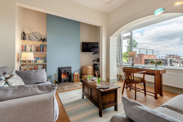 A living room with a fireplace, bookshelves, a TV, and a dining area with a view of the city. - 5 Bed in Studland (oc-wy365) (Studland)