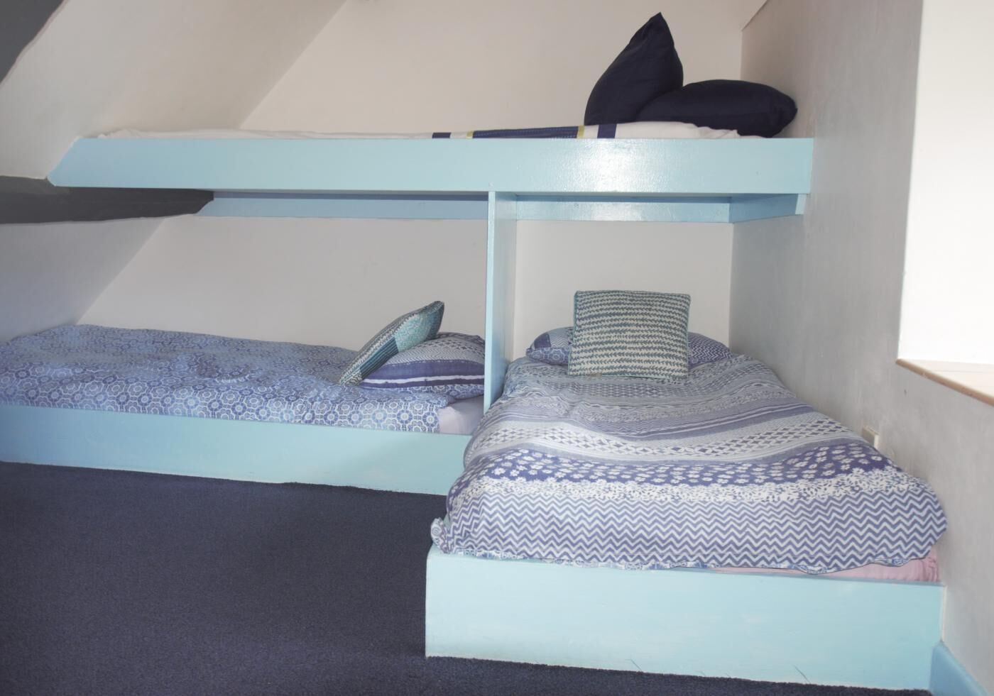 A dormitory room with two bunk beds, each with patterned bedding and pillows.