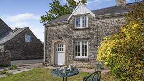 A stone house with a white door, a small porch, and a table with chairs in the front yard. - 2 Bed in St. Hilary (oc-c33064) (Cowbridge)