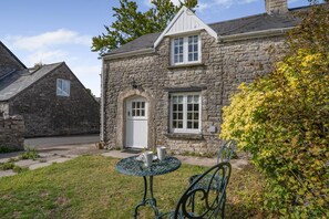 Ein Haus aus Stein mit einer weißen Tür, einer kleinen Veranda und einem Tisch mit Stühlen im Vorgarten.