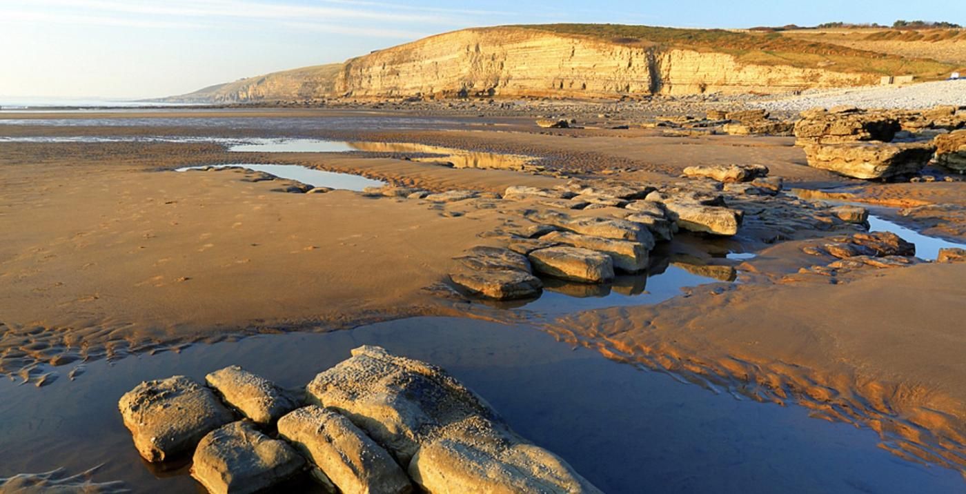 Un paysage côtier avec une plage de sable, des affleurements rocheux et des falaises en arrière-plan.