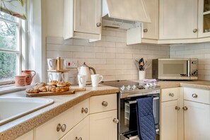 A kitchen with white cabinets, a microwave, a stove, and a window with a view of trees. - 2 Bed in St. Hilary (oc-c33064) (Cowbridge)