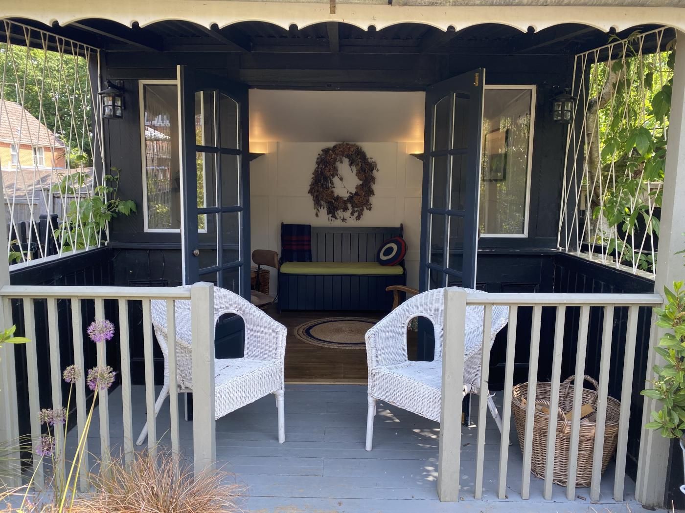 A covered porch with two white wicker chairs, a bench, and a decorative wreath.