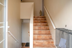 Eine Treppe mit Handlauf, eine Tür mit Klinke und ein an der Wand befestigtes Nummernschild.