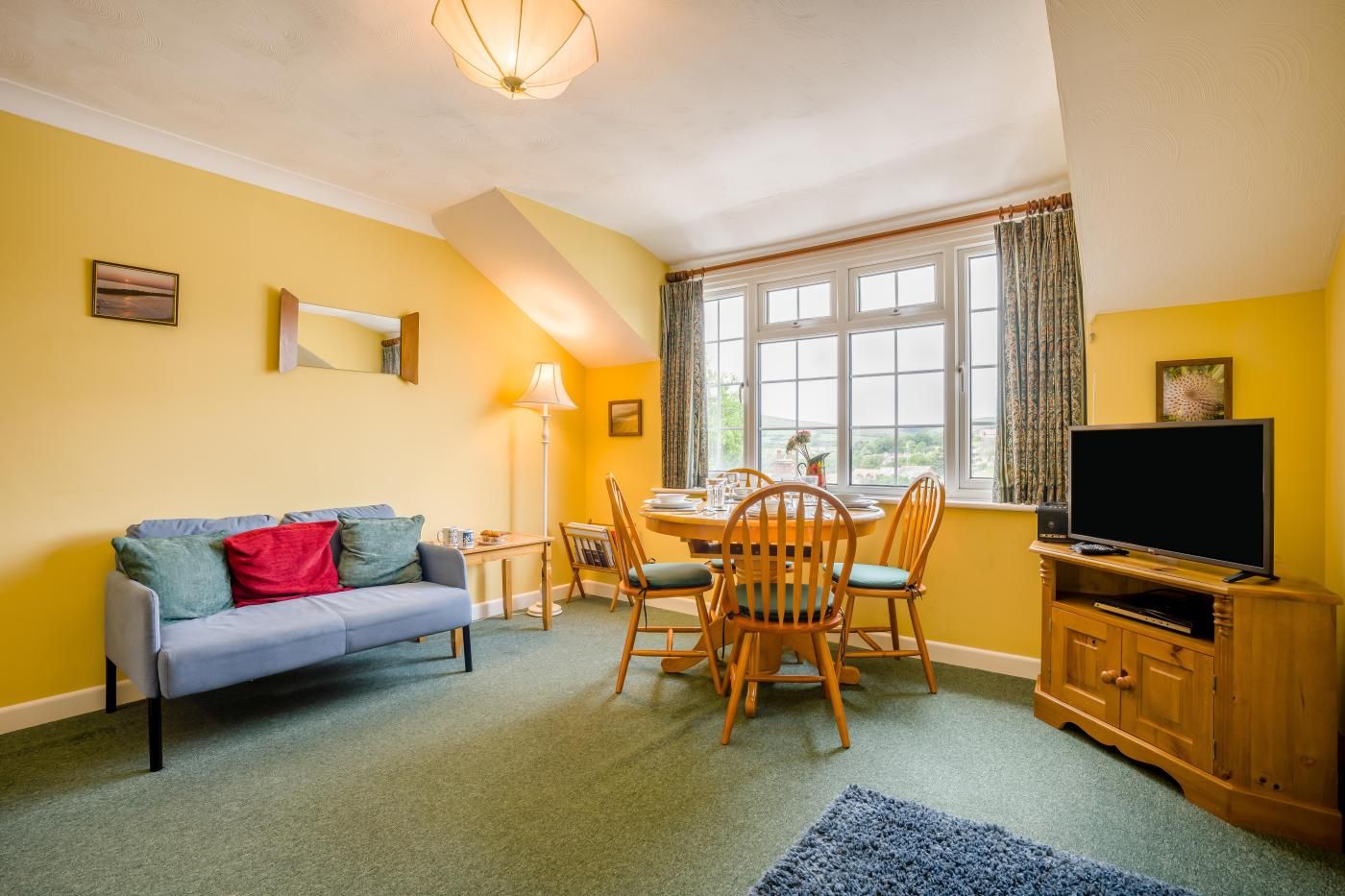 Ein Wohnzimmer mit einer Couch, einem Esstisch, Stühlen, einem Fernseher und einem Fenster mit Vorhängen.