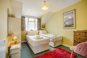 Une chambre avec deux lits simples, une commode en bois, un tapis rouge et une affiche accrochée au mur.