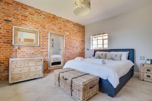 A bedroom with a brick wall, a bed with white bedding, a dresser, a mirror, and a window. - 2 Bed in Halesworth (oc-bbs) (Bramfield)