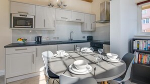 Una cocina moderna con armarios blancos, un microondas y una estufa. Hay una mesa de comedor dispuesta con platos, vasos y cubiertos.