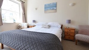 A bedroom with a large bed, bedside tables, a chair, a painting, and a window. - 1 Bed in Swanage (oc-wy413) (Swanage)