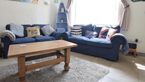 A living room with a sofa, a coffee table, a bookshelf, and a painting on the wall. - 1 Bed in Swanage (oc-wy413) (Swanage)