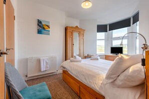 Um quarto com cama, radiador, televis ão, janela com vista e um quadro na parede.