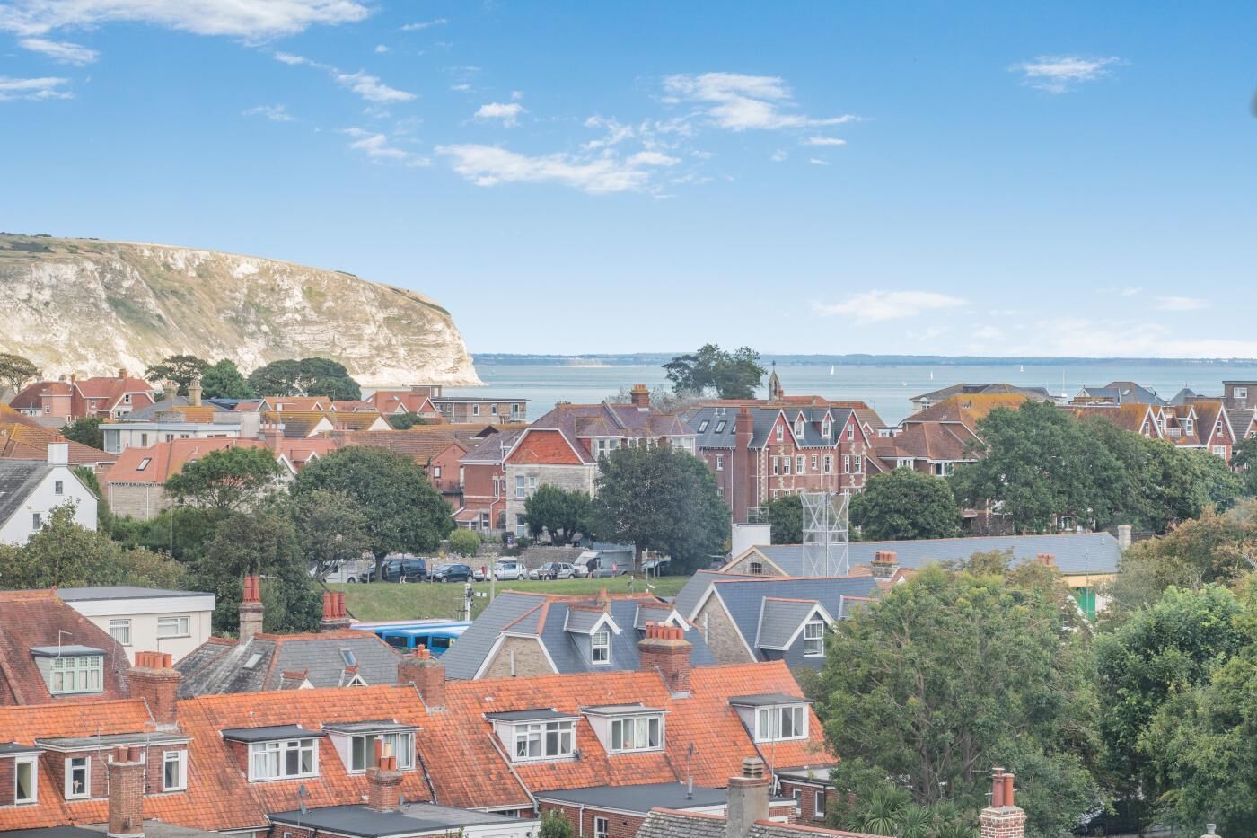 A coastal town with red-roofed houses, a prominent cliff, and a view of the sea.