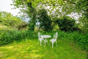 Un jardin avec une table et des chaises en métal blanc, entouré d’une végétation luxuriante.