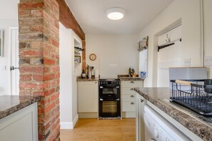 A kitchen with a brick wall, white cabinets, a built-in oven, and a countertop with a dish rack. - 2 Bed in Saxmundham (oc-rvr) (Snape)