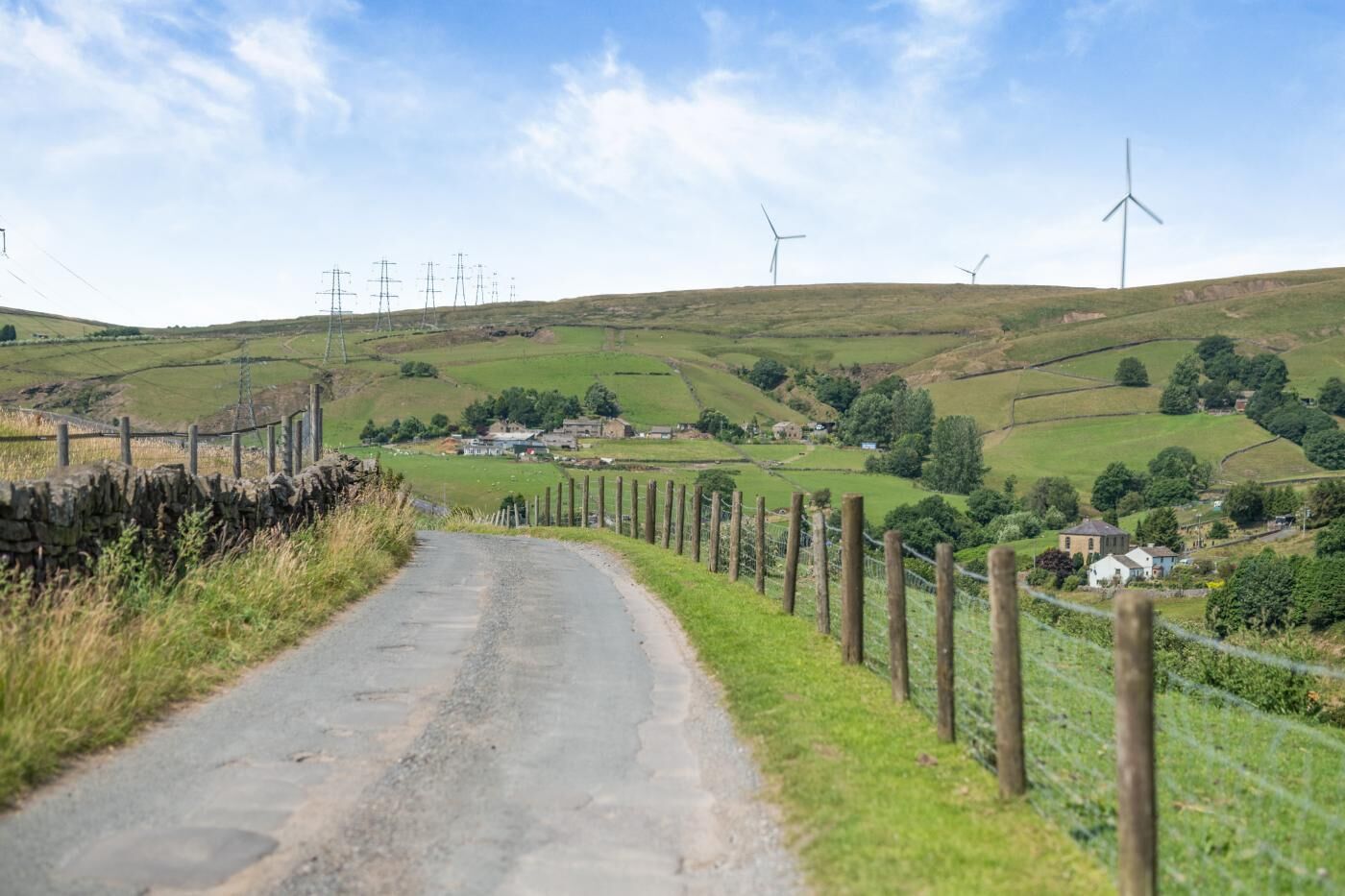 Eine ländliche Straße mit Windkraftanlagen im Hintergrund.