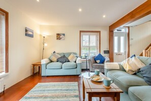 Un salon chaleureux avec un canapé, une table basse et un fauteuil à rayures. Il y a une fenêtre avec des stores, une lampe et un tableau au mur.
