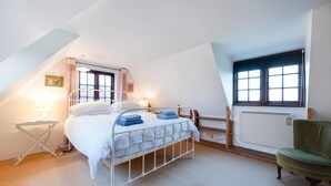 Ein Schlafzimmer mit Bett, Nachttischen, einem Sessel, einem Fenster und einer Heizung.