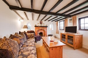 Un salon chaleureux avec une cheminée, un ensemble de canapés, une table en bois et un téléviseur posé sur un meuble en bois.