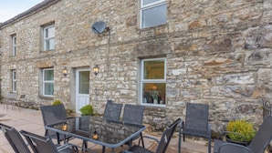 A stone building with outdoor seating, including a table and chairs, and a door.