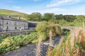 A stone building with a stone bridge over a stream, surrounded by greenery. - 4 Bed in Hawes (oc-t33084) (High Abbotside)