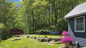 Une maison avec un jardin bien entretenu, une caravane rouge et un arbuste à fleurs roses.