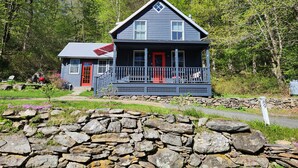 A two-story house with a porch, a red door, and a stone wall in front.