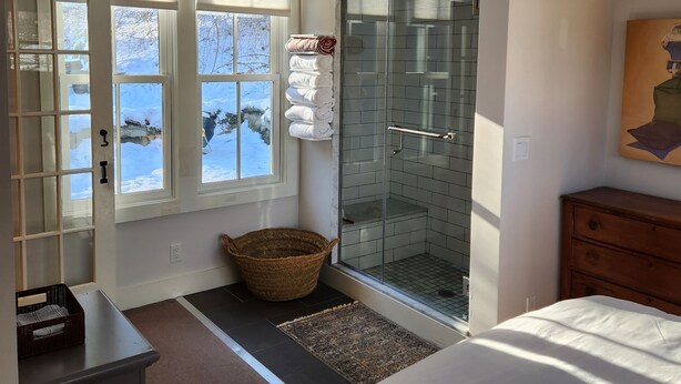Une chambre avec un grand lit, une commode en bois, une cabine de douche en verre et une vue sur un paysage enneigé par les fenêtres.