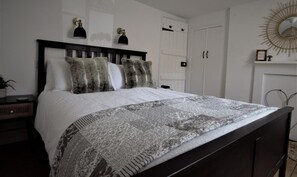 A neatly made bed with a patterned bedspread and two pillows, a bedside table with a lamp, and a wall-mounted light fixture. - 2 Bed in Swanage (oc-wy460) (Swanage)