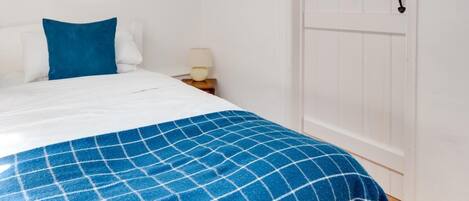 A bedroom with a bed, a blue checkered blanket, a white door, and exposed wooden beams on the ceiling.
