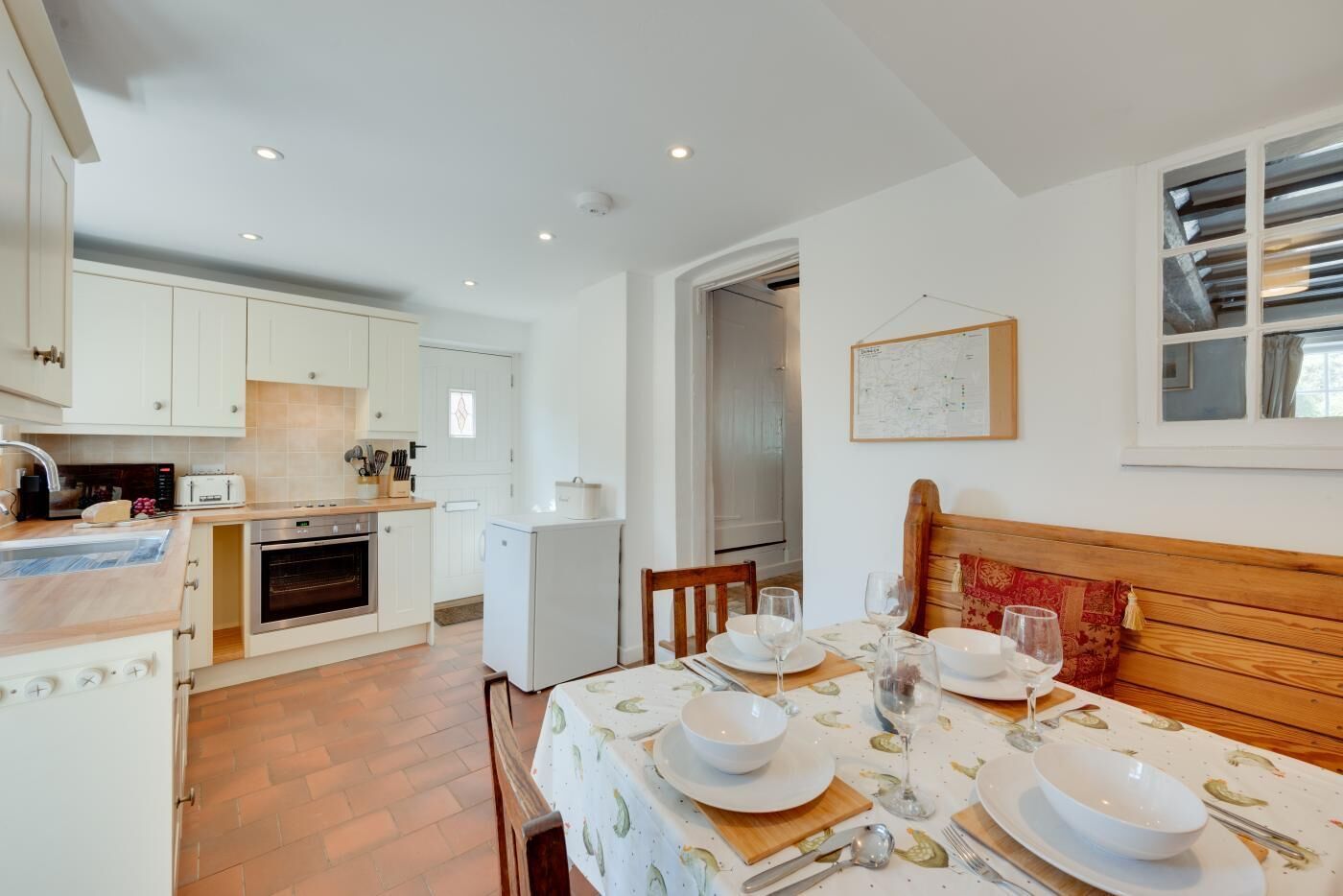 A compact kitchen with modern appliances, a dining area with a wooden bench, and a map on the wall.