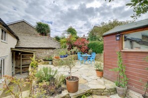 A stone patio with blue chairs, a small table, and potted plants. - 2 Bed in Swanage (oc-wy382) (Swanage)