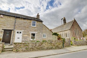 A stone building with a traditional design, featuring a prominent church with a steeple and a small adjacent house with a stone facade and a wooden door. - 2 Bed in Swanage (oc-wy382) (Swanage)