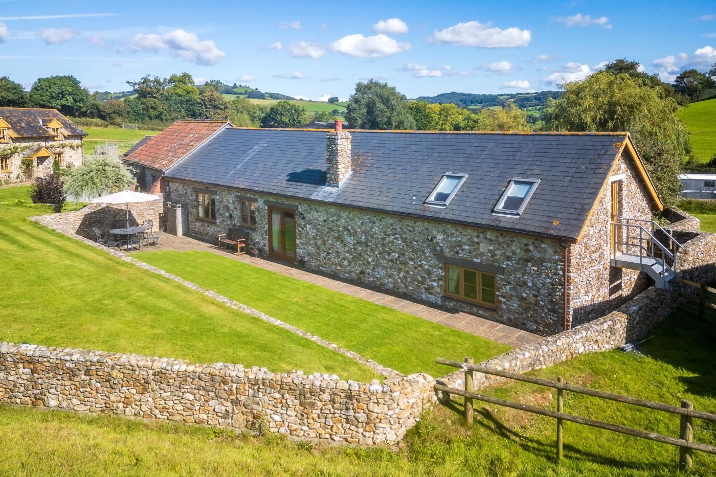 A stone farmhouse with a sloped roof, a stone wall, and a grassy yard.