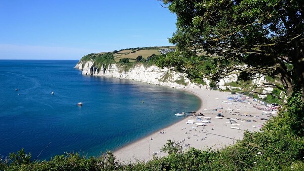 Una spiaggia costiera con scogliere bianche, mare cristallino e ombrelloni.