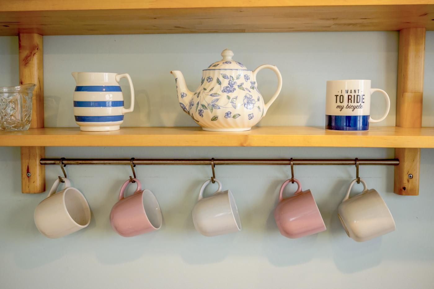 Een plank met een theepot, een mok en een ophangrek met kopjes.