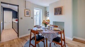 A dining area with a round table set for four, a chandelier, and a view of the kitchen. - 2 Bed in Whitstable (oc-o32772) (Whitstable)