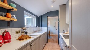 A modern kitchen with a long countertop, wooden shelves, and a window above the sink. - 2 Bed in Whitstable (oc-o32772) (Whitstable)